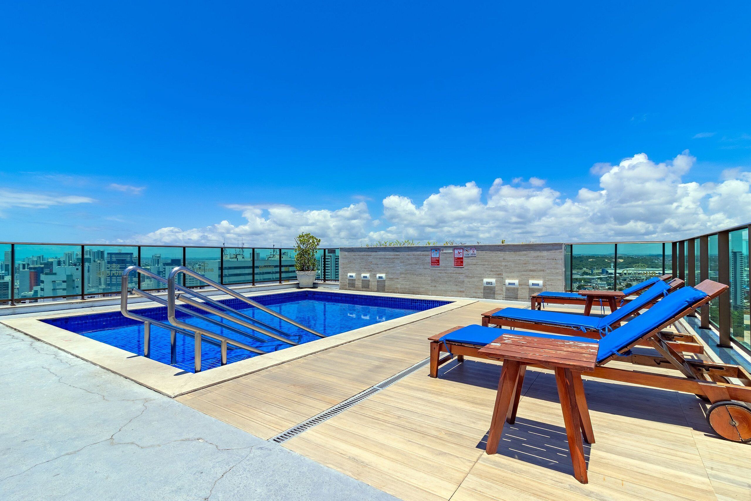Ein Poolbereich auf dem Dach mit freiem Blick auf die Skyline der Stadt, Holzliegen und einem Pool mit Metallleiter.
