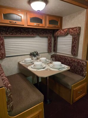 Ein kompaktes Wohnmobil-Interieur mit Esstisch für vier Personen, umgeben von gepolsterten Sitzgelegenheiten.