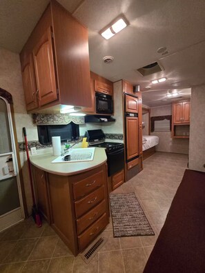 A compact kitchen with wooden cabinets, a microwave, stove, and a refrigerator. - Peaceful rv near moody gardens and galveston (La Marque)
