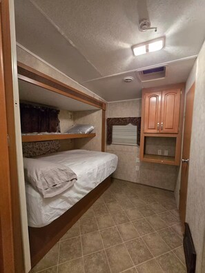 Ein kompaktes Wohnmobil-Interieur mit einer Etagenbett, einer kleinen Küchenzeile und einem Deckenventilator.