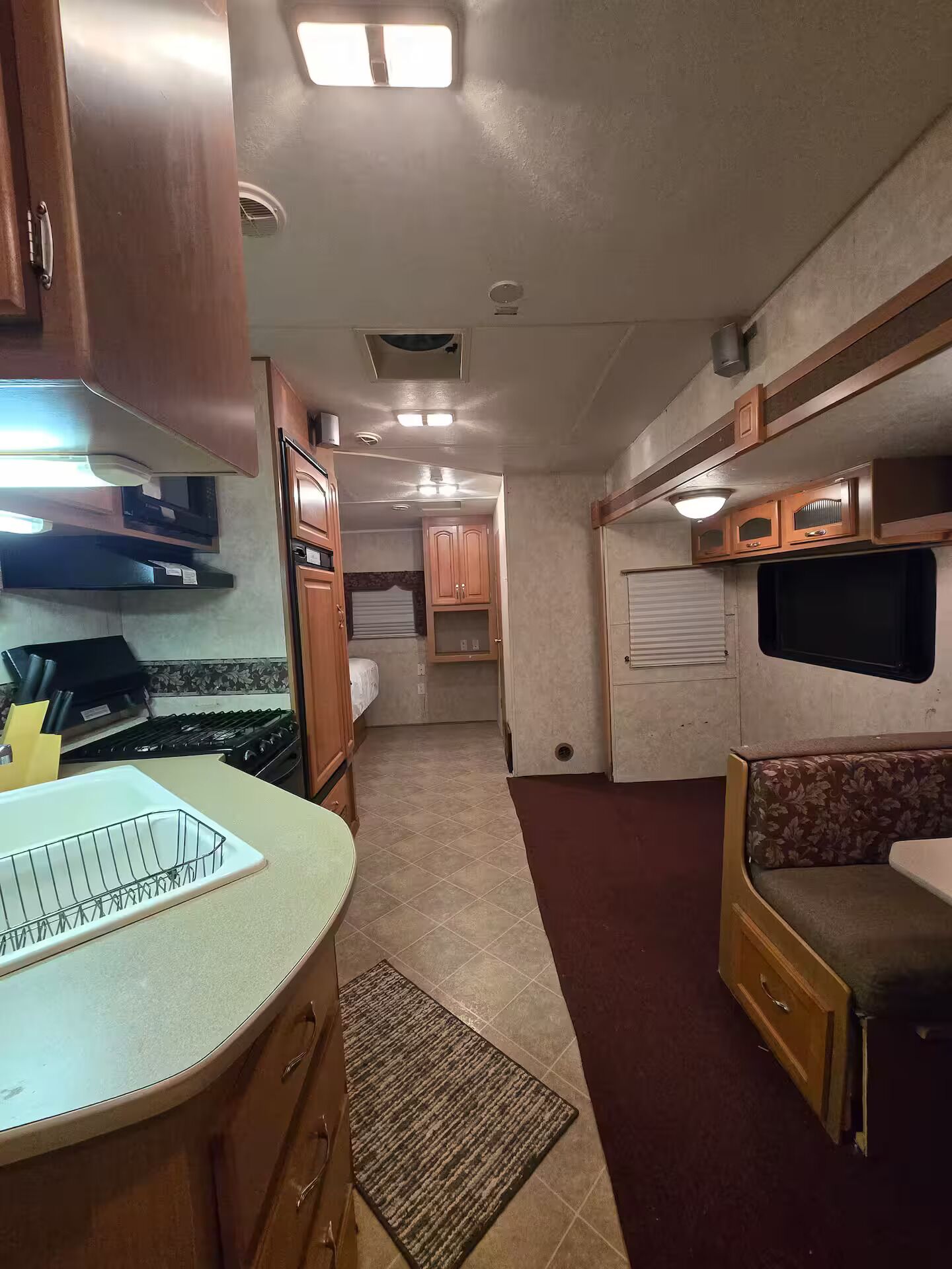 A compact RV interior with a kitchenette, a seating area, and a small sleeping space.