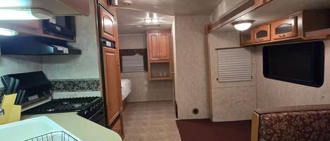 A compact RV interior with a kitchenette, a seating area, and a small sleeping space.