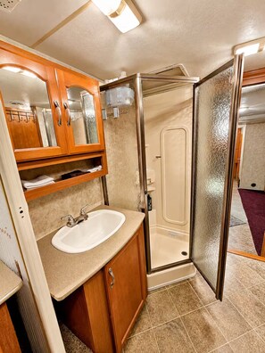 Baño compacto para autocaravana con lavamanos, espejo y ducha.