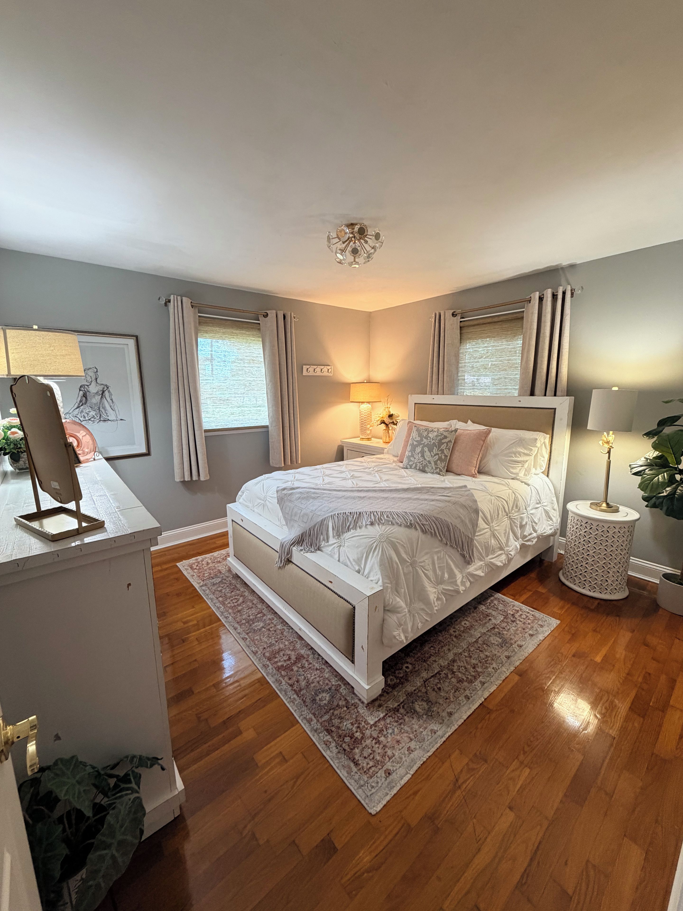 A bedroom with a bed, bedside lamps, a desk, and a window with curtains.
