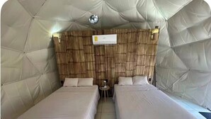 Ein Zimmer mit zwei Betten, einer Wandklimaanlage und einem kleinen Tisch mit Lampe.