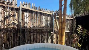 Ein Whirlpool, umgeben von einem Bambuszaun und einer überdachten Struktur mit einem Reetdach.