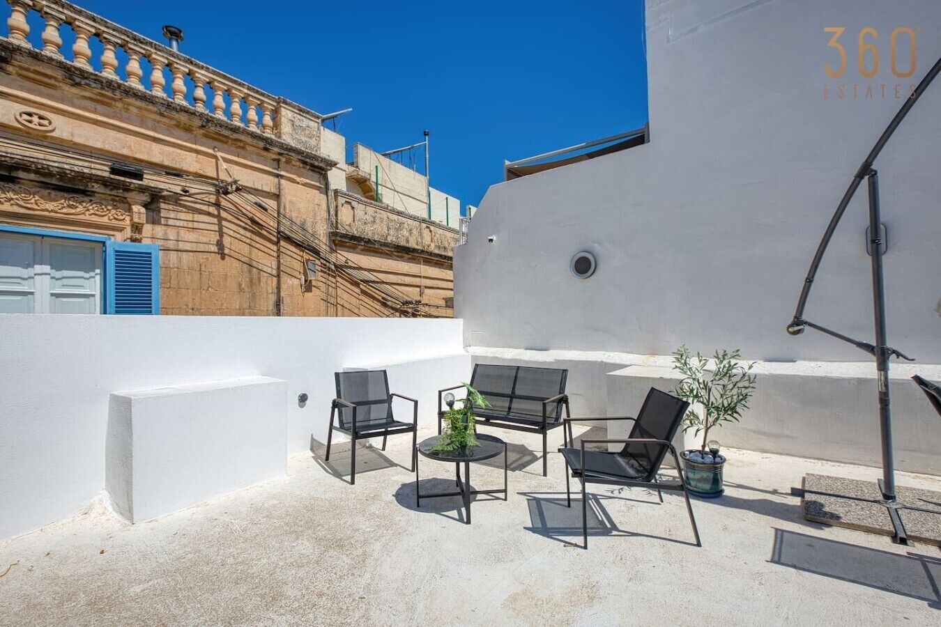 Une terrasse sur le toit, avec des sièges en plein air, un pot de fleurs et une vue dégagée sur les bâtiments environnants.
