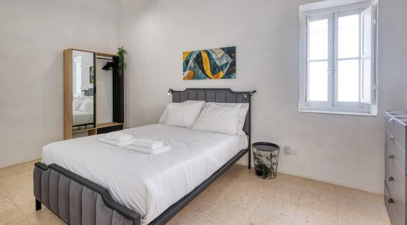 A bedroom with a bed, a mirror, a painting, a window, and a dresser.
