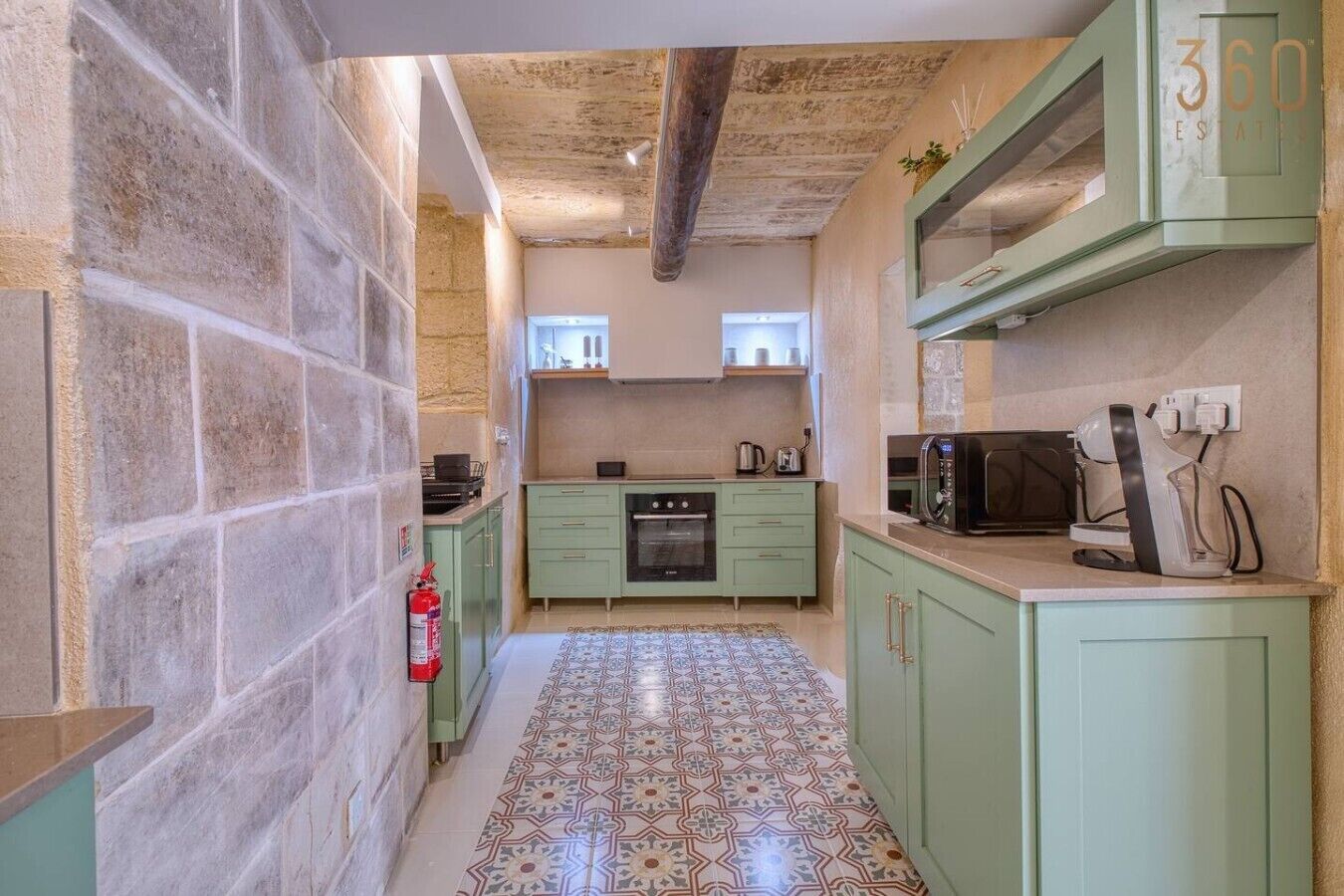 Uma cozinha pequena com piso de azulejos, armários verdes, micro-ondas e um extintor de incêndio.