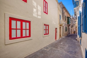 Eine schmale Straße mit Gebäuden an beiden Seiten, mit roten Fensterrahmen und einem gepflasterten Gehweg.