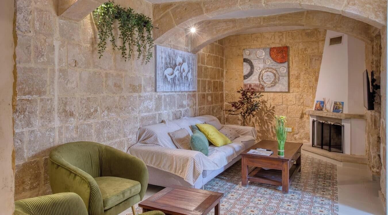 A cozy living room with a stone wall, a sofa, a green armchair, a coffee table, and a fireplace.