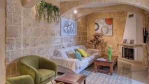 A cozy living room with a stone wall, a sofa, a green armchair, a coffee table, and a fireplace. - Beautiful 2BR home in Rabat with rooftop Terrace (Rabat)