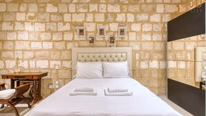A hotel room with a stone wall, a bed with white linens, a wooden nightstand, and a chair. - Beautiful 2BR home in Rabat with rooftop Terrace (Rabat)