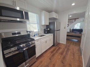 A modern kitchen with stainless steel appliances, a wooden floor, and a staircase leading to a living area. - Tidemark Row | Stylish Coastal Getaway (Atlantic City)