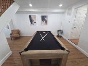 A pool table with cue sticks, a chair, and two abstract paintings on the wall. - Tidemark Row | Stylish Coastal Getaway (Atlantic City)