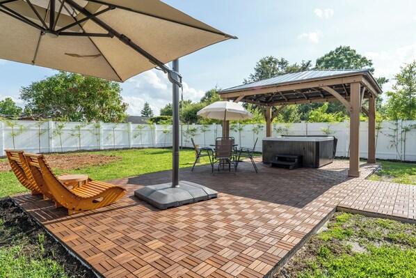 Ulkoterassi, jossa on pergola, puinen pöytä, tuoleja ja grilli.