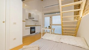 A bedroom with a bed, a wooden ladder, a kitchen in the background, and a window. - Clit1: Bright Loft Near Loreto (Milano)