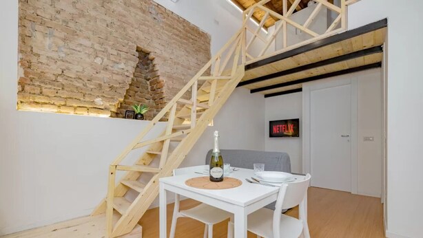 A dining area with a white table, chairs, a wooden staircase, a brick wall, and a Netflix sign. - Clit1: Bright Loft Near Loreto (Milano)