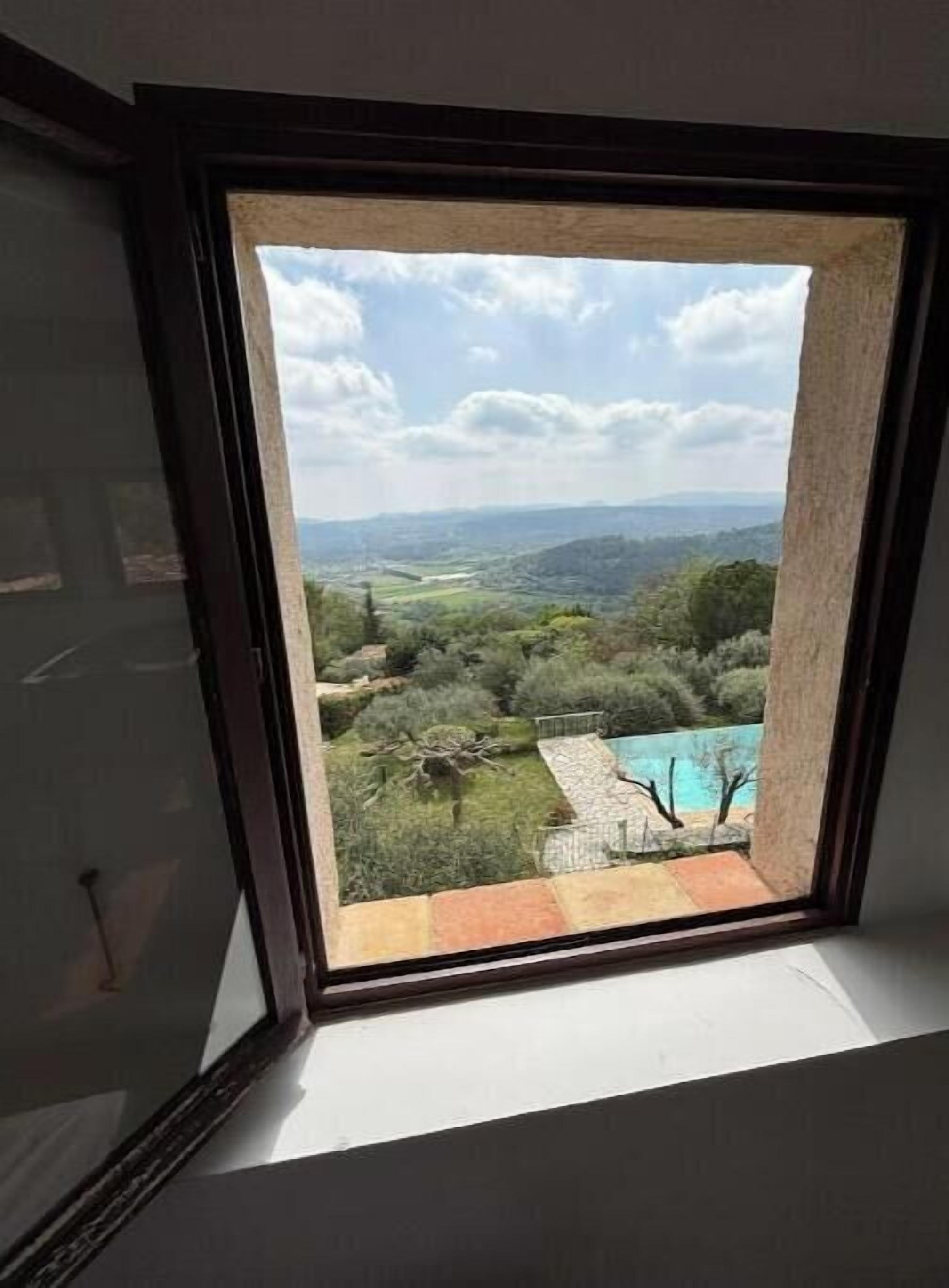 A window with a view of a swimming pool and surrounding greenery.
