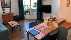 A modern living room with a wooden dining table, a sofa, a TV mounted on the wall, and a window with curtains. - Bright studio apartment with a small terrace (Viroflay)