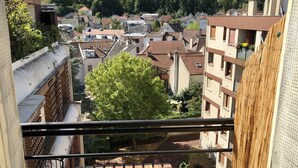 A balcony with a wooden table and chairs, overlooking a residential area with various buildings and a forested hill in the background. - Bright studio apartment with a small terrace (Viroflay)