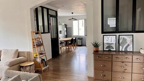 Un salon moderne comprenant un canapé, une bibliothèque en forme d’échelle en bois, un coin repas avec une table et des chaises, et une cuisine équipée d’un réfrigérateur et de placards.