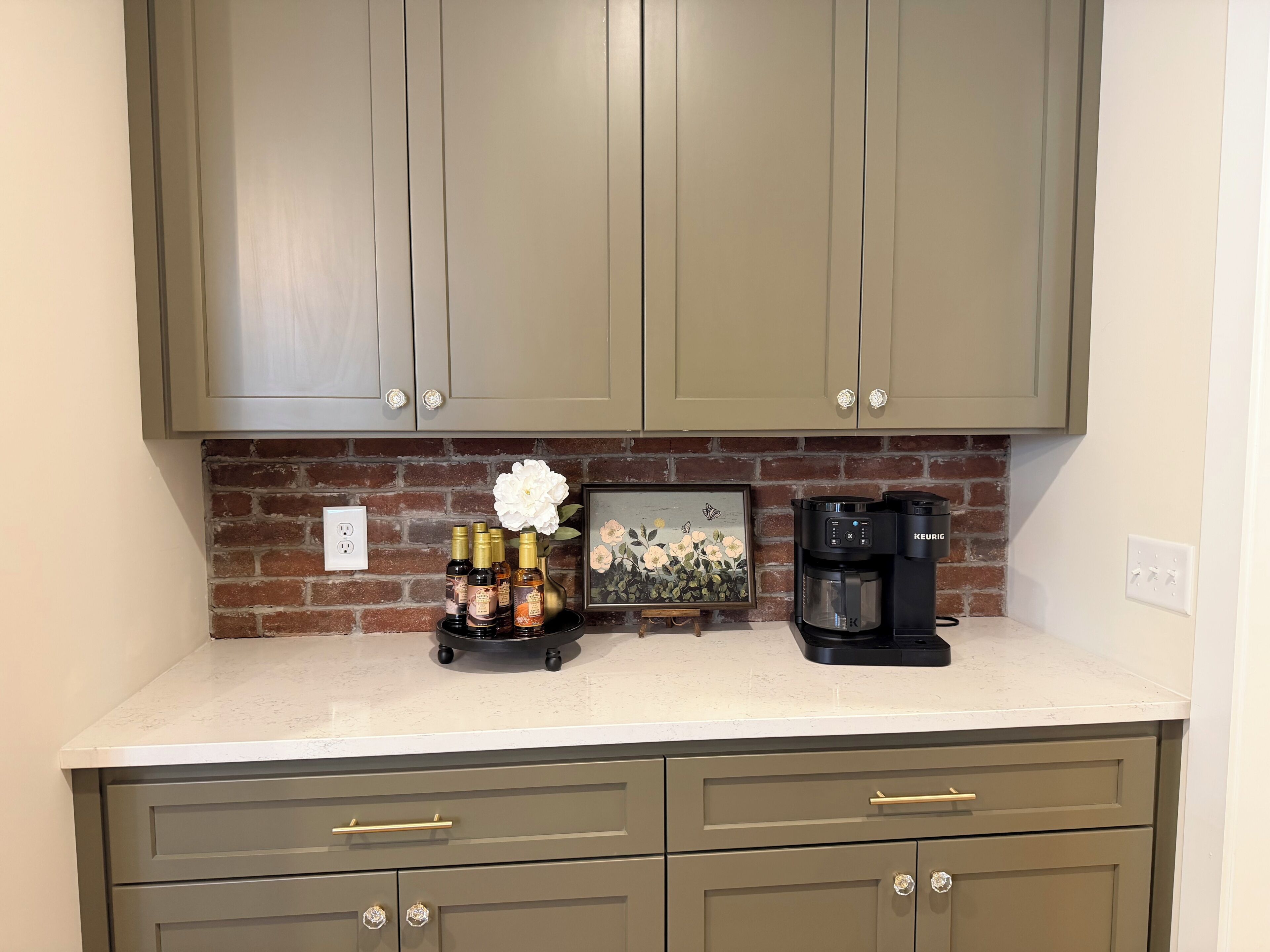 A kitchen with a brick backsplash, a coffee maker, and a decorative vase with flowers.