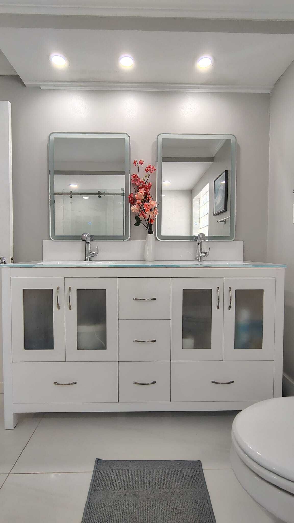 Un baño moderno con un tocador blanco, dos espejos, un lavamanos y un inodoro.