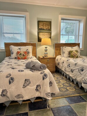 A bedroom with two beds, a nightstand with a lamp, and artwork on the wall. - The Beach Club | Classic AB Cottage by The Circle (Atlantic Beach)
