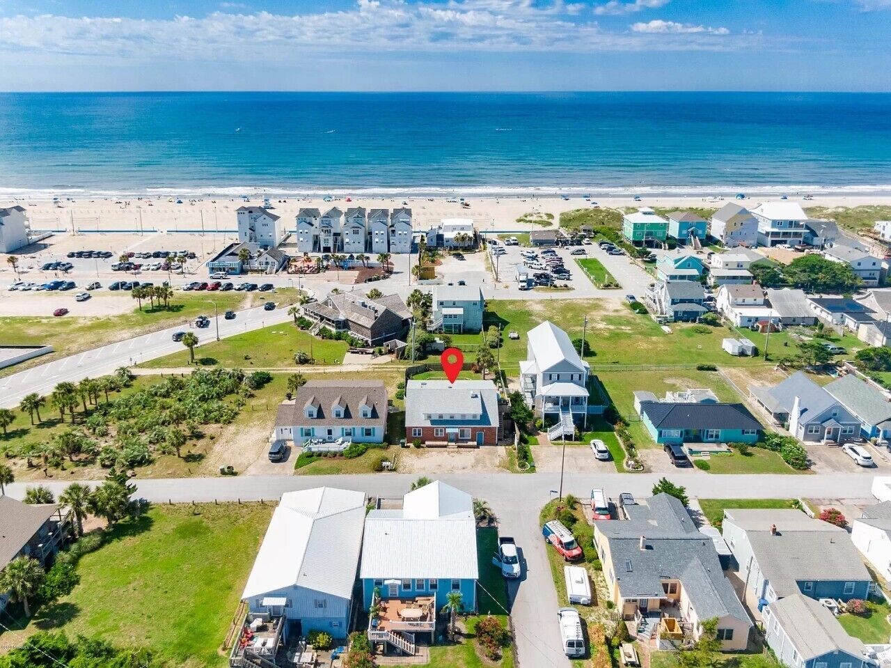 An aerial view of a coastal residential area with houses, a beach, and a parking lot.