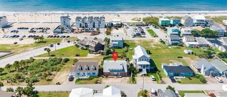 An aerial view of a coastal residential area with houses, a beach, and a parking lot.