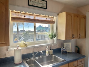 A kitchen with a window, sink, wooden cabinets, and a view of a building. - The Beach Club | Classic AB Cottage by The Circle (Atlantic Beach)