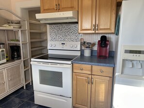 Una cocina compacta con estufa blanca, armarios de madera, cafetera y dispensador de agua.