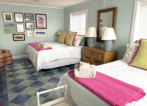 Un dormitorio con dos camas, un aparador de madera, una silla y una pared decorada con marcos.