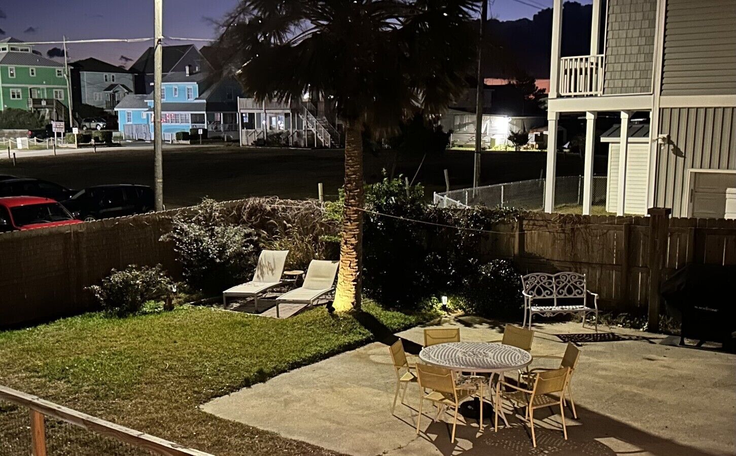 A backyard with a lawn, a palm tree, and outdoor furniture including a table and chairs.
