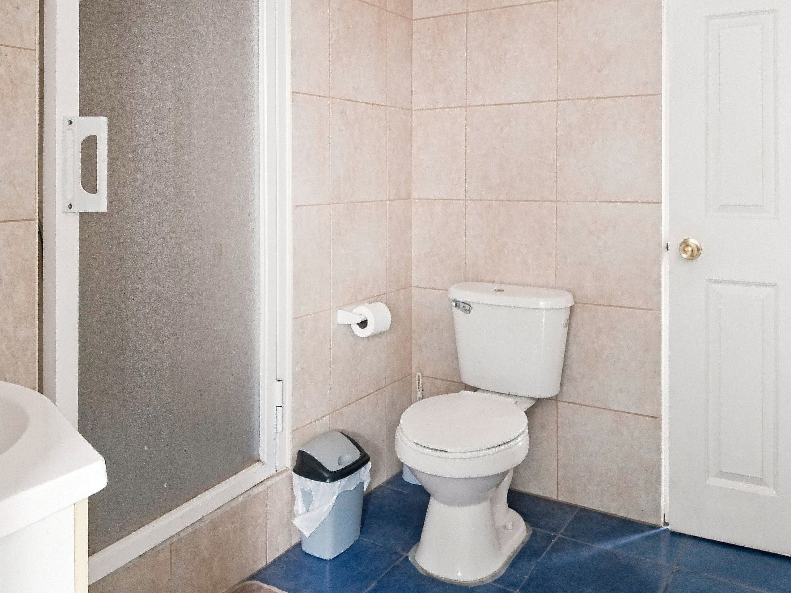 Une salle de bain comprenant des toilettes, une poubelle et un espace douche.