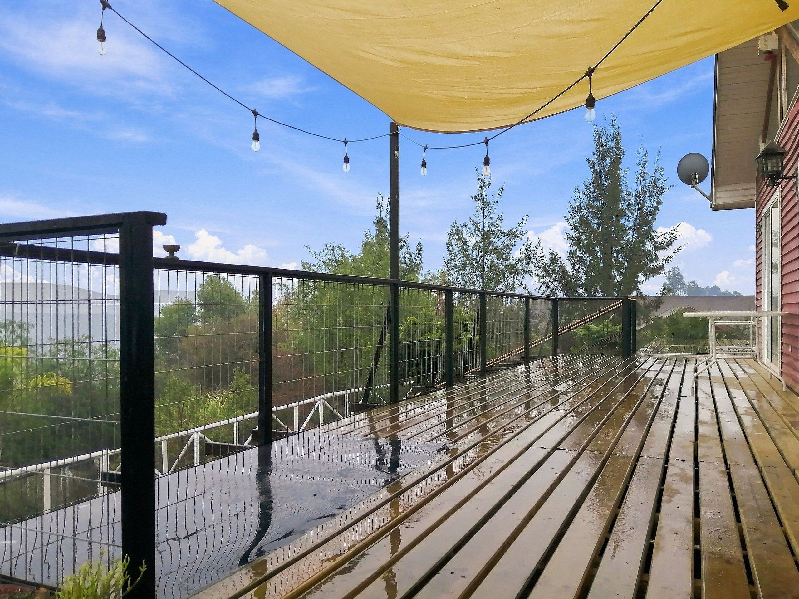 Une terrasse en bois avec une rambarde en métal, un auvent jaune et des guirlandes lumineuses.