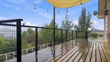 Une terrasse en bois avec une rambarde en métal, un auvent jaune et des guirlandes lumineuses.