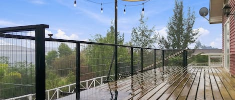 Una terraza de madera con barandilla de metal, un dosel amarillo y luces colgantes.