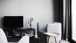 A modern living room with a flat-screen TV, a grey armchair, a small wooden side table, and a bookshelf. - Aurum ApartHotels Città Studi (Milano)