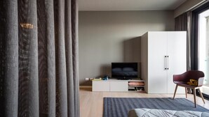 A modern bedroom with a bed, a TV on a white cabinet, a red chair, and a large window. - Aurum ApartHotels Città Studi (Milano)
