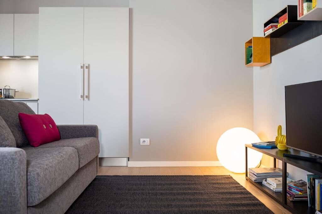 A modern living room with a grey sofa, a red pillow, a black coffee table, a bookshelf, and a large round light fixture.