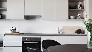 A modern kitchen with white cabinetry, a black oven, a wooden cutting board, and a vase with flowers. - Aurum ApartHotels Città Studi (Milano)