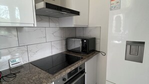 A kitchen with white cabinets, a black microwave, a stove, and a refrigerator. - Tulip Suite at Elmwood House (Nottingham)