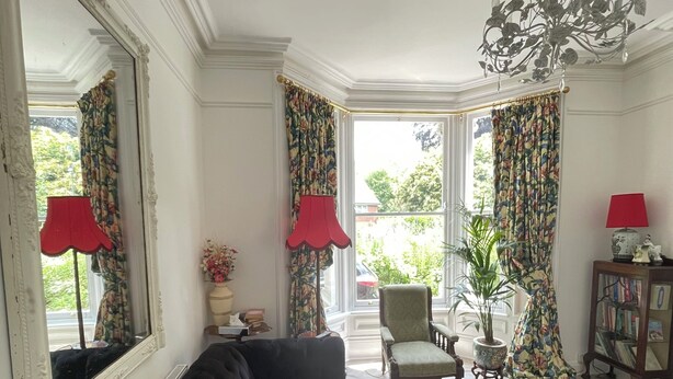A room with a black sofa, a large mirror, a chandelier, and a view of greenery outside. - Tulip Suite at Elmwood House (Nottingham)