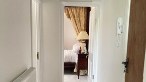 A hallway leading to a bedroom with a bed, a bedside lamp, and a telephone. - Tulip Suite at Elmwood House (Nottingham)
