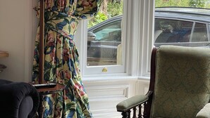 A room with a large window, a green armchair, a red lamp, and a floral curtain. - Tulip Suite at Elmwood House (Nottingham)