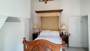 A bedroom with a four-poster bed, a chandelier, two bedside tables with lamps, and a door. - Tulip Suite at Elmwood House (Nottingham)