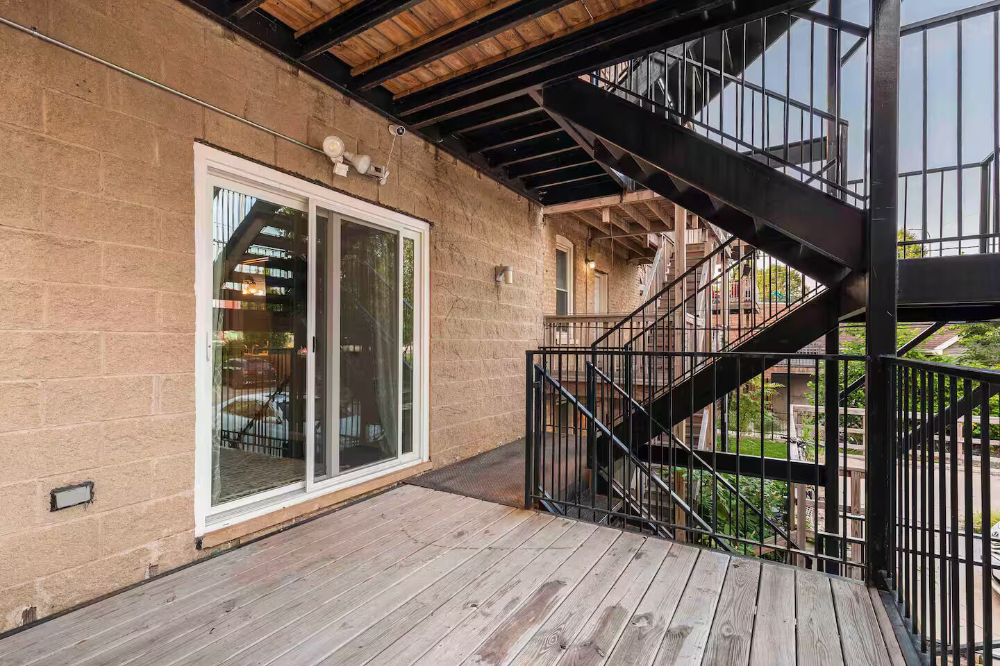 A wooden deck with a metal staircase leading to a balcony.