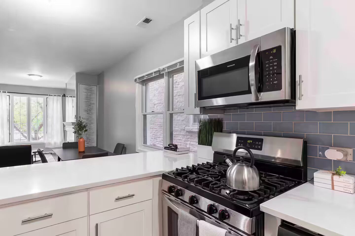 A modern kitchen with white cabinetry, a stainless steel stove, a microwave, and a gas range.
